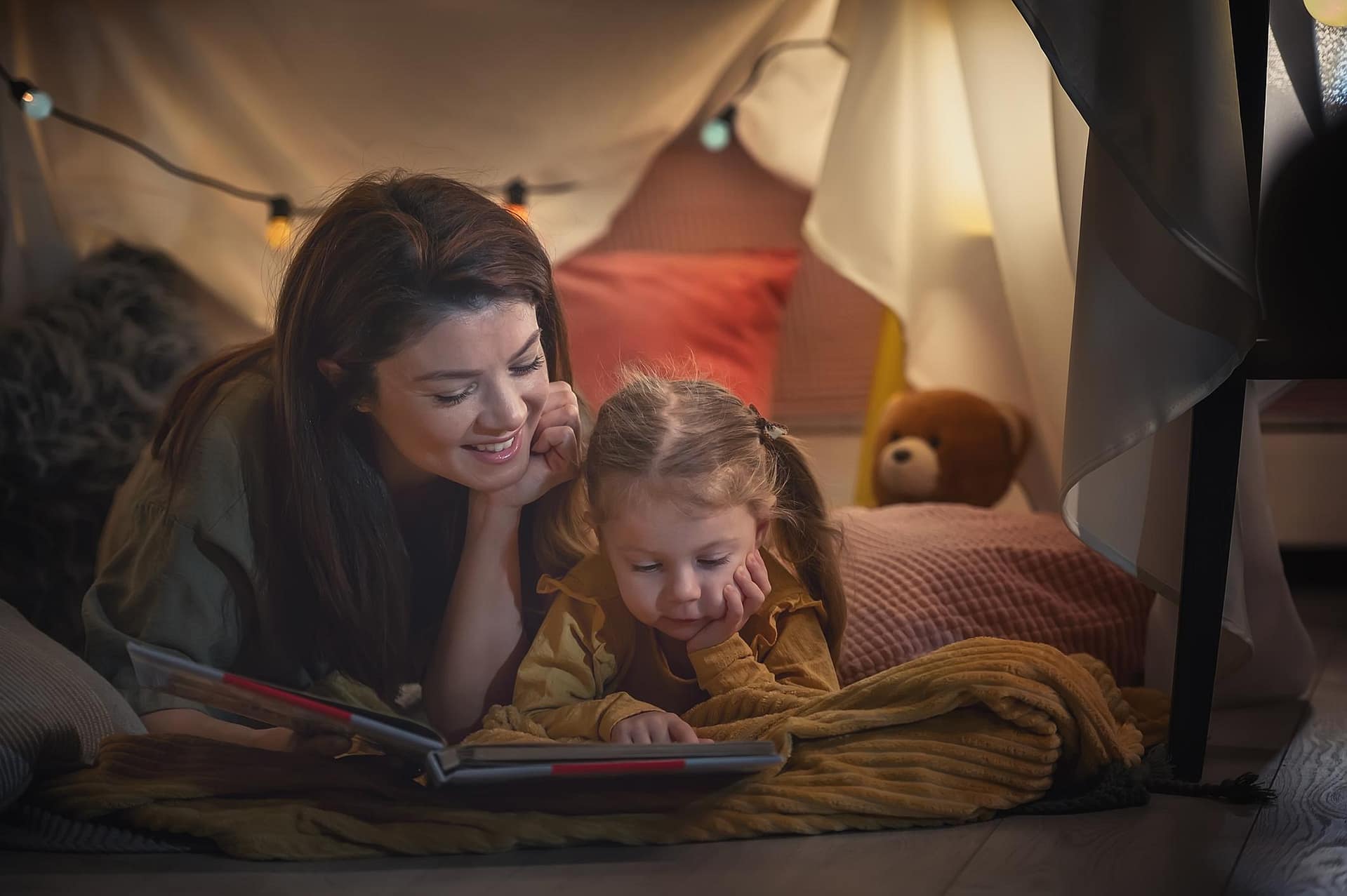 Storytelling for Emotional Healing and Emotional Development. parents with kids reading story book under tent house